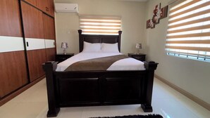Un dormitorio con cama, armario de madera, mesitas de noche y ventana con persianas.