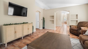 Een woonkamer met een flatscreen televisie, een houten kast, een bruine leren bank en een kamerkleed met een patroon.
