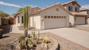 Een woonhuis met garage, omgeven door een tuin met cactussen en rotsen.