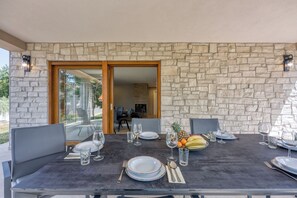 A dining area with a stone wall, a glass door leading to a room, and a table set for four with plates, glasses, and cutlery. - Secluded Pool Villa Tanja /w Sea View, Marasi, Croatia (Marasi)