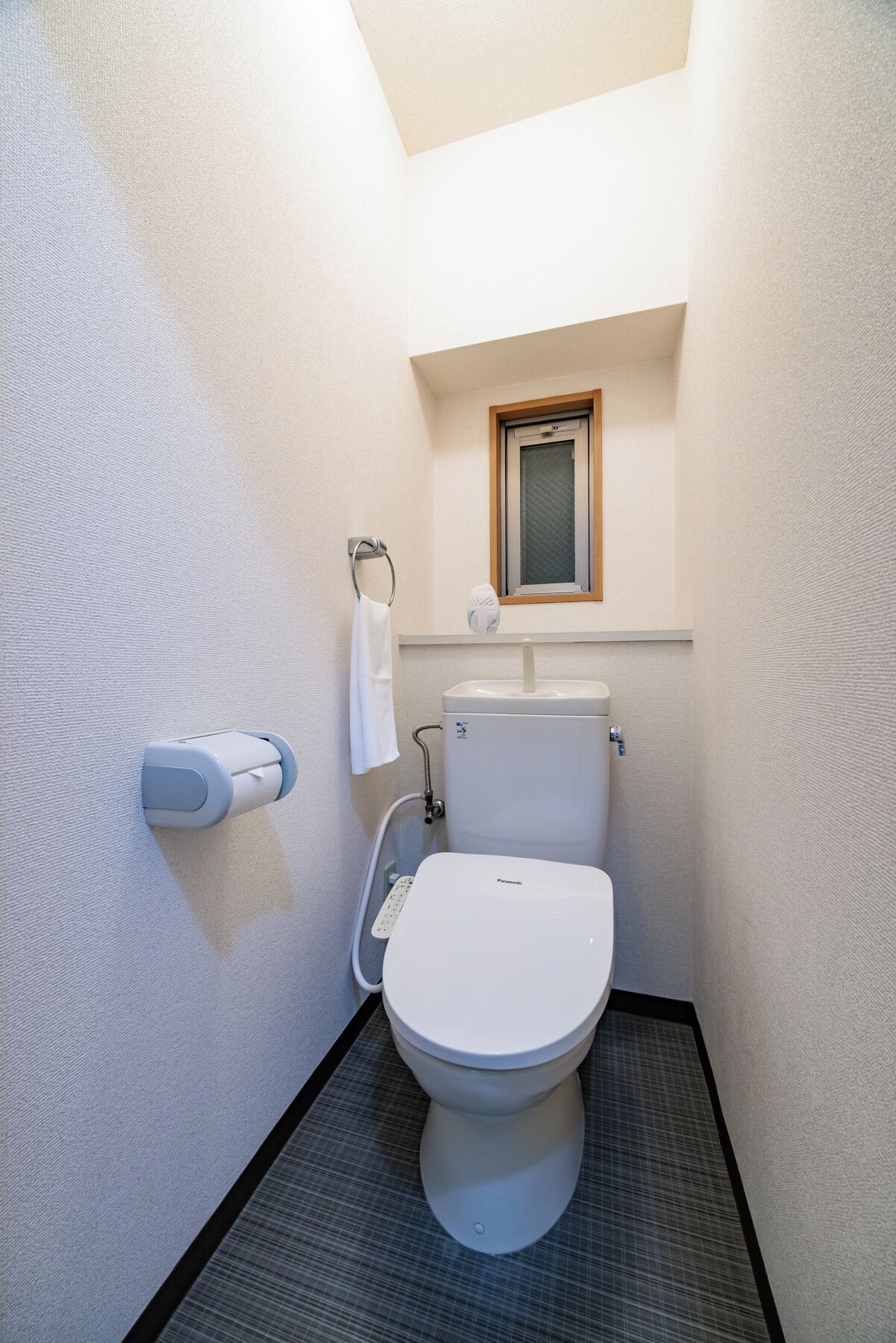 A compact bathroom with a toilet, a hand dryer, and a towel rack.