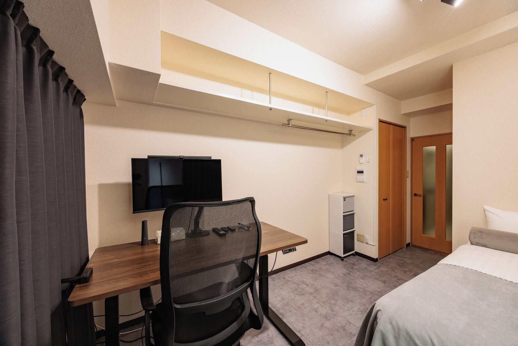 A hotel room with a desk, chair, television, wardrobe, and bed.