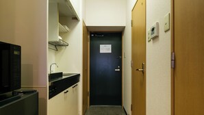 Ein schmales Entree mit einer Küchenzeile links, einer dunklen Tür am Ende und einer Holztür rechts.
