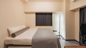 Ein Hotelzimmer mit Bett, Schreibtisch, Stuhl, Klimaanlage und einem Fenster mit Vorhängen.