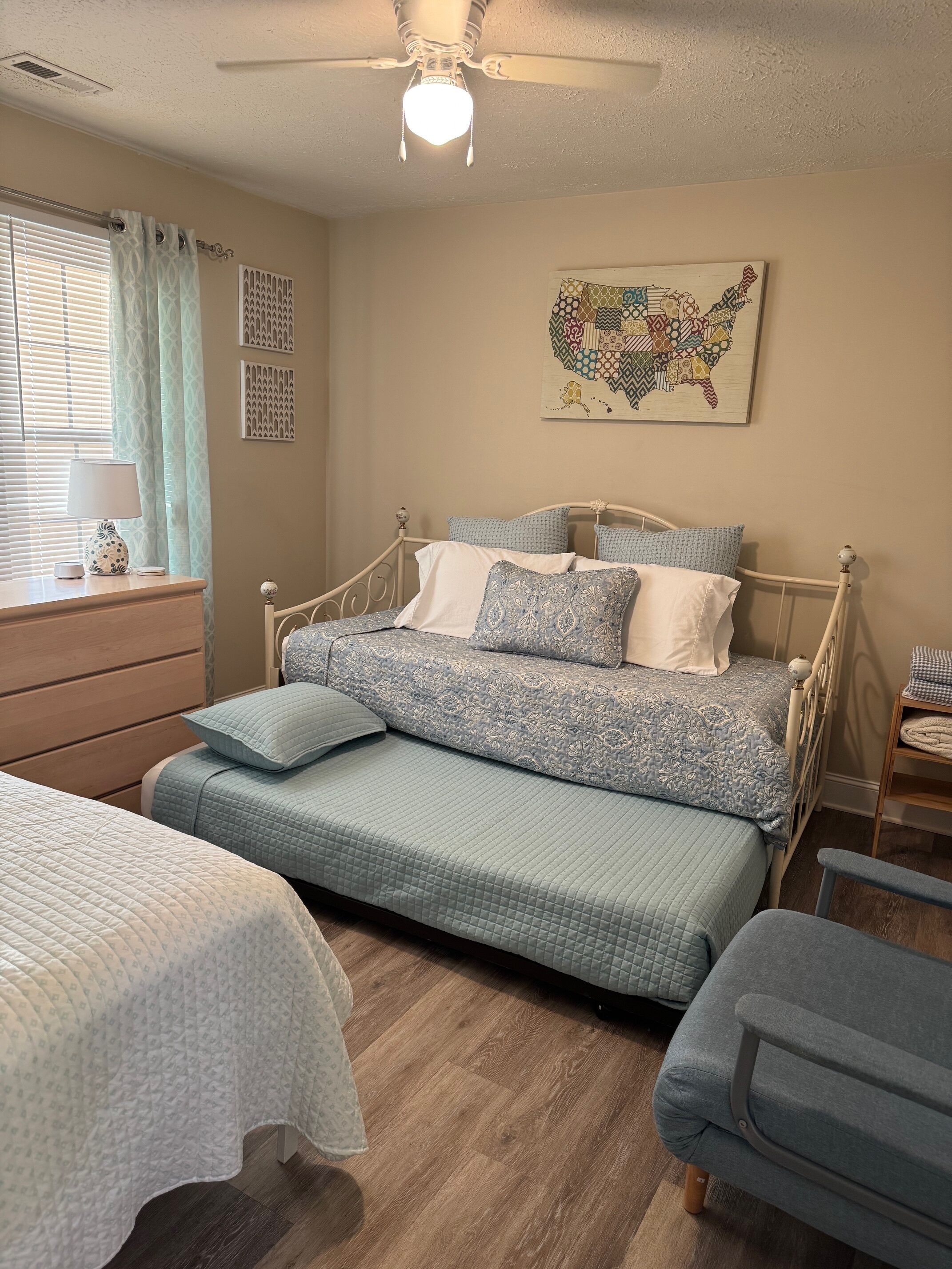 Een slaapkamer met een bed, bureau, stoel en plafondventilator.