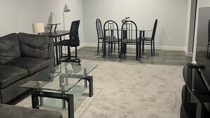 Un salon moderne avec un canapé gris, une table basse en verre et un coin repas comprenant une table et des chaises.