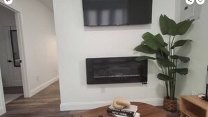 Un salon moderne avec une table basse en bois, deux œuvres d’art encadrées accrochées au mur, une plante en pot et une petite bibliothèque.