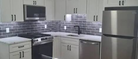 A modern kitchen with light-colored cabinets, a stainless steel refrigerator, a built-in oven, and a microwave.