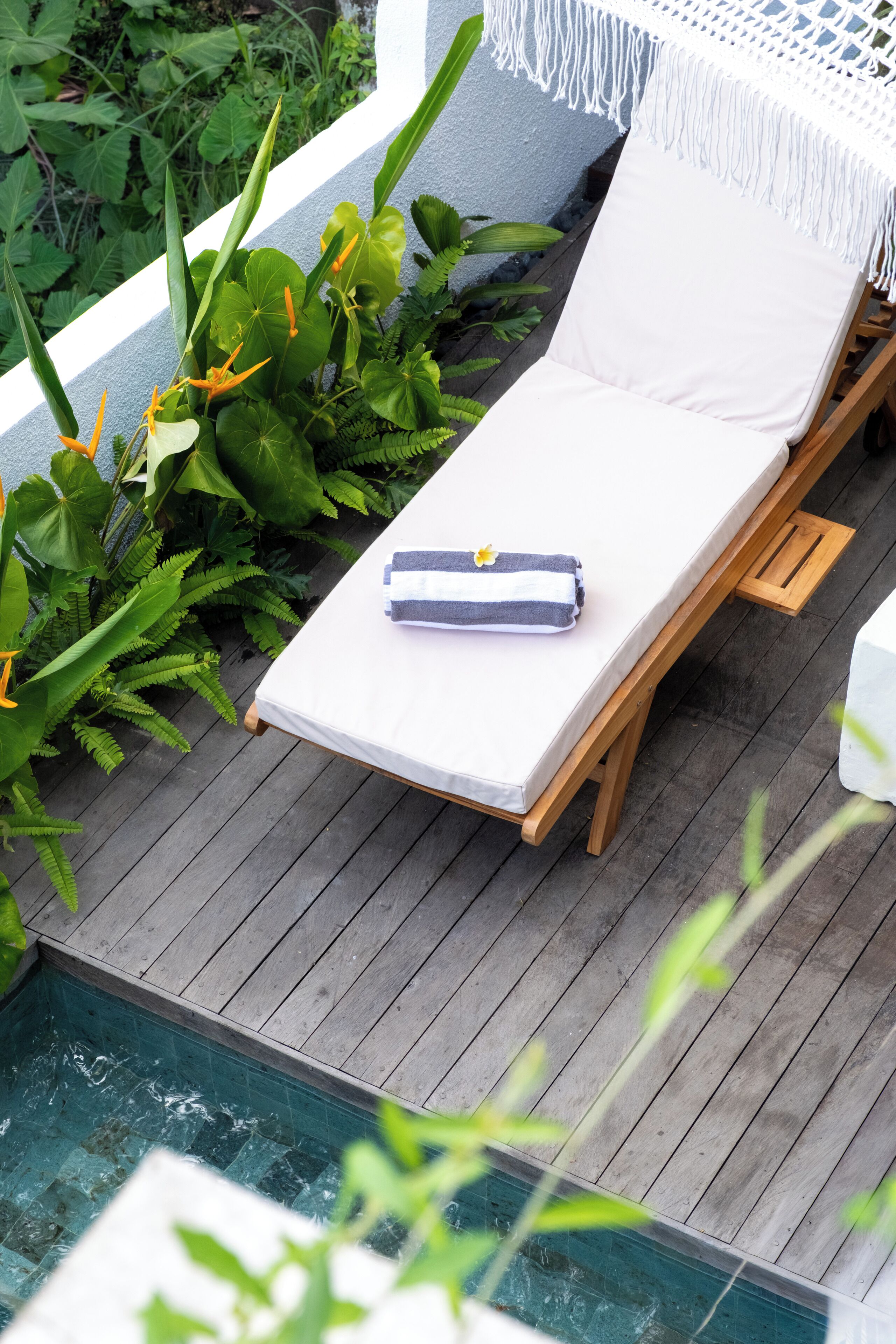 A wooden deck with a white lounge chair, a small table, and a pool.