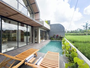 A modern house with a swimming pool, wooden deck, and a view of a lush green field.