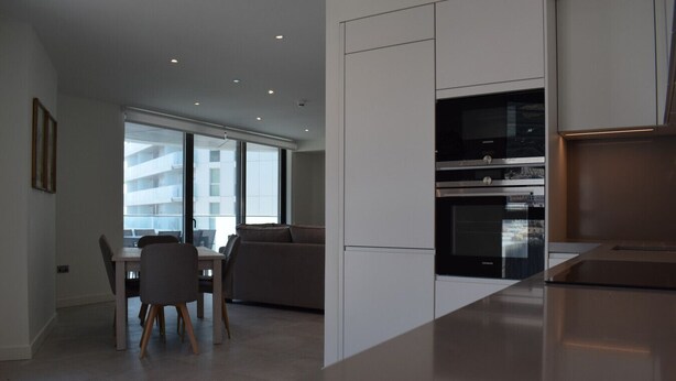 Een moderne keuken met inbouwapparatuur, een eethoek met tafel en stoelen, en grote ramen die zorgen voor natuurlijk licht.
