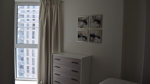Een slaapkamer met een raam, een witte dressoir en twee abstracte schilderijen aan de muur.