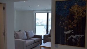 Een moderne woonkamer met een grijze bank, een salontafel en een groot raam met uitzicht op de stad.