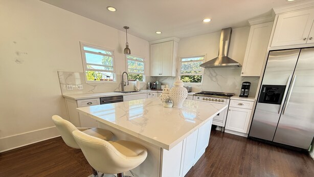 A modern kitchen with a large island, white cabinetry, stainless steel appliances, and a bar stool. - La Jolla White Door Cottage walking distance to beach, cove, shops, &restaurants (La jolla)