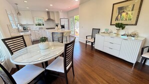A modern kitchen with white cabinetry, a marble island, and a dining area with a round table and chairs. - La Jolla White Door Cottage walking distance to beach, cove, shops, &restaurants (La jolla)