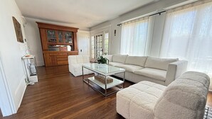 A modern living room with a glass coffee table, white sofas, and a wooden cabinet in the background. - La Jolla White Door Cottage walking distance to beach, cove, shops, &restaurants (La jolla)
