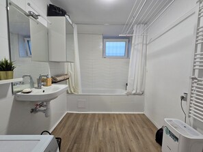 Une salle de bain moderne équipée d’un lavabo, d’un miroir, d’un porte-serviettes, d’une douche et d’une fenêtre.