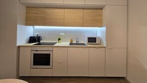 A compact kitchen with white cabinets, a microwave, a kettle, and a small sink.