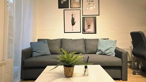 A living room with a grey sofa, a coffee table, and a potted fern. There are framed pictures on the wall.