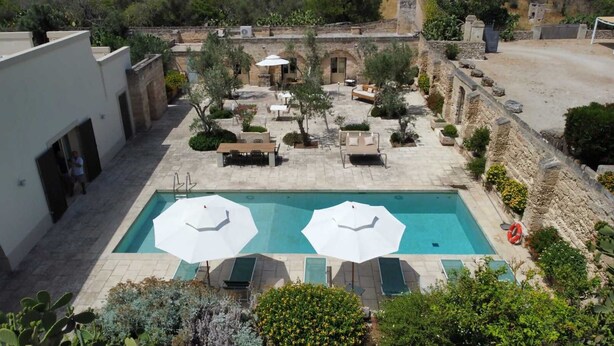 Un espace piscine aménagé sur le toit, avec deux parasols, des sièges d’extérieur et un mur en pierre.
