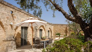 Un bâtiment en pierre doté d’un patio comprenant une table et des chaises, le tout abrité par un parasol blanc.