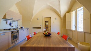A spacious kitchen with a long wooden table, red chairs, and a bowl of fruit.