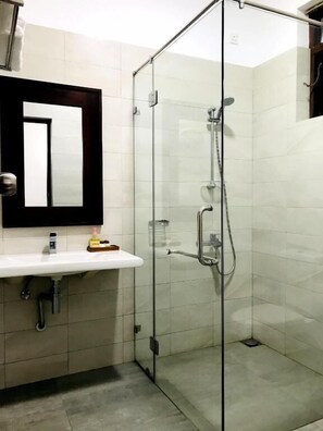 A modern bathroom with a glass-enclosed shower, a white sink with a mirror above it, and tiled walls. - Siluni's Villa (Anuradhapura)