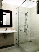 A modern bathroom with a glass-enclosed shower, a white sink with a mirror above it, and tiled walls.