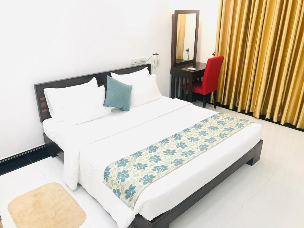 A neatly made bed with white and blue bedding, a red chair, and a mirror on a dark wooden nightstand.