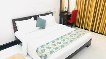 A neatly made bed with white and blue bedding, a red chair, and a mirror on a dark wooden nightstand.