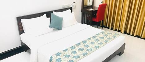 A neatly made bed with white and blue bedding, a red chair, and a mirror on a dark wooden nightstand.