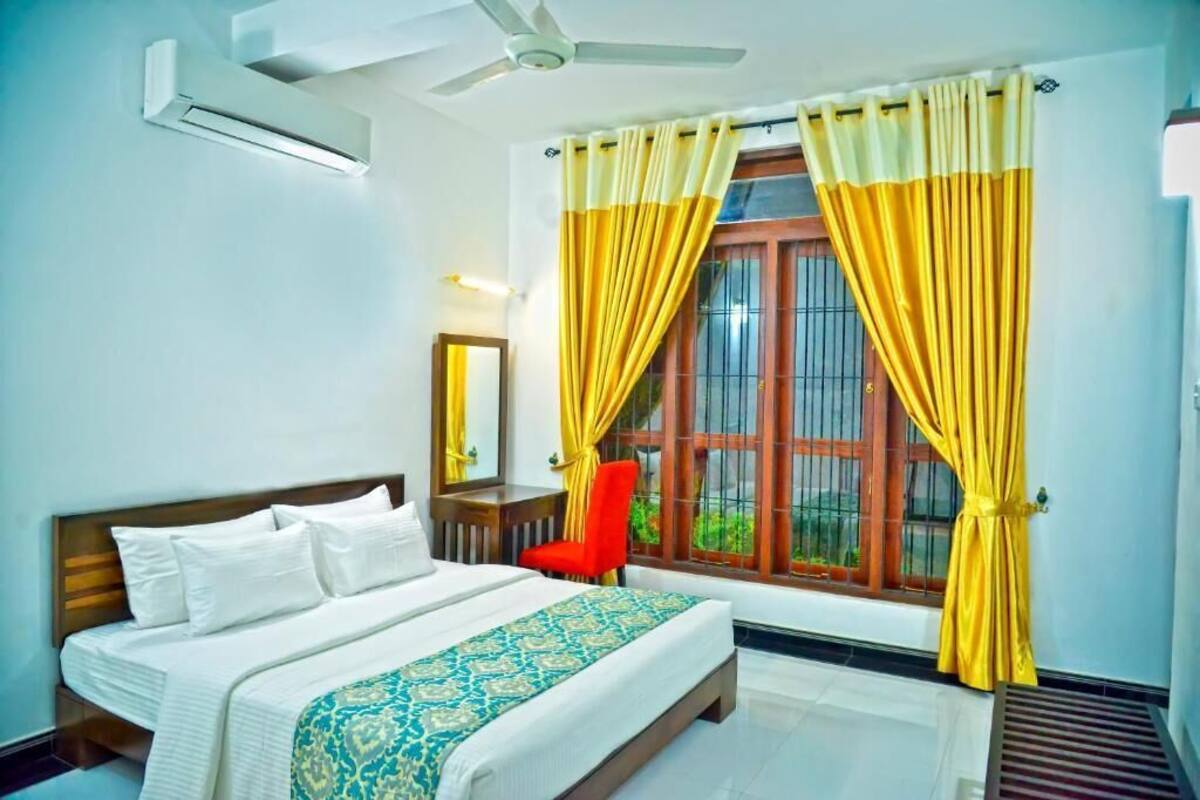 A hotel room with a bed, a red chair, a ceiling fan, and yellow curtains.