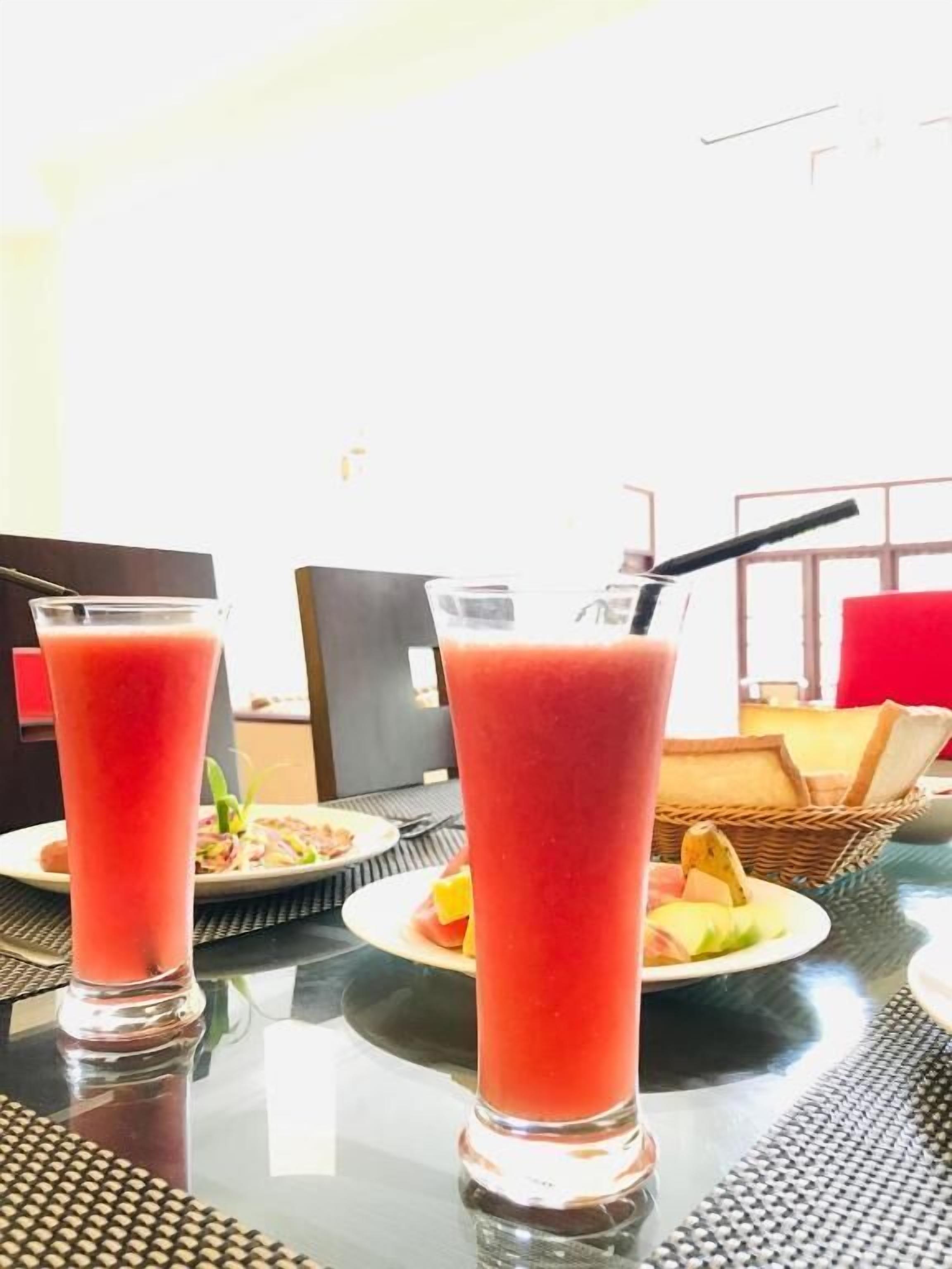 Two tall glasses of red beverage on a table with plates of food and a basket.