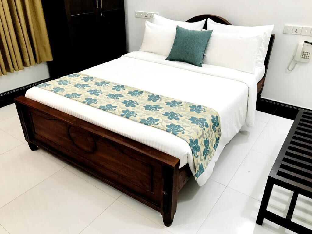 Una cama bien hecha con colcha estampada, cabecera de madera y teléfono en la mesita de noche.
