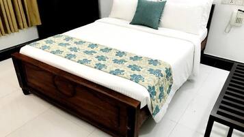Una cama bien hecha con colcha estampada, cabecera de madera y teléfono en la mesita de noche.