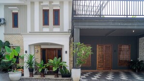 Una casa moderna de dos pisos con piso a cuadros, un porche con plantas en macetas y un garaje con puerta de madera.
