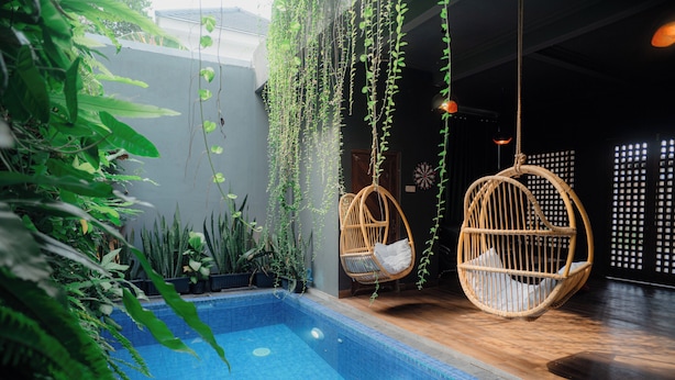 Zona de piscina con sillones colgantes, plantas en macetas y suelo de baldosas.