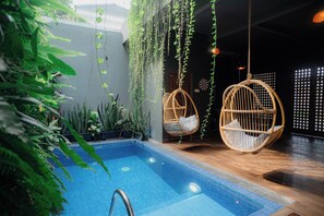 A pool area with hanging chairs, potted plants, and a tiled floor. - Illusion Homestay (Ngaglik)