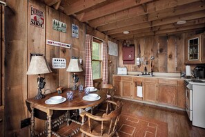 L’intérieur d’une cabane en bois comprend une table à manger pour quatre personnes, une cuisine avec des meubles en bois et divers panneaux décoratifs sur les murs.