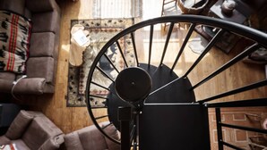 A spiral staircase with a black metal railing, a brown leather sofa, and a patterned rug in a room with wooden flooring and a window.