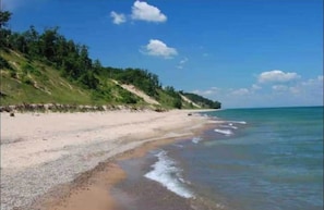 Een strand met een zandrijk strand en zachte golven, begrensd door een grasachtige heuvel.