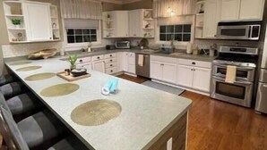 A modern kitchen with white cabinets, a large island with bar stools, stainless steel appliances, and recessed ceiling lighting.