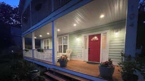 A two-story house with a covered porch, a red door, and potted plants.