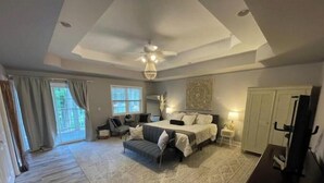 A spacious bedroom with a large bed, a ceiling fan, and a view through the window.