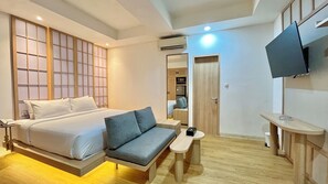 Una habitación de hotel moderna con cama, sofá, mesita, televisor y espejo.
