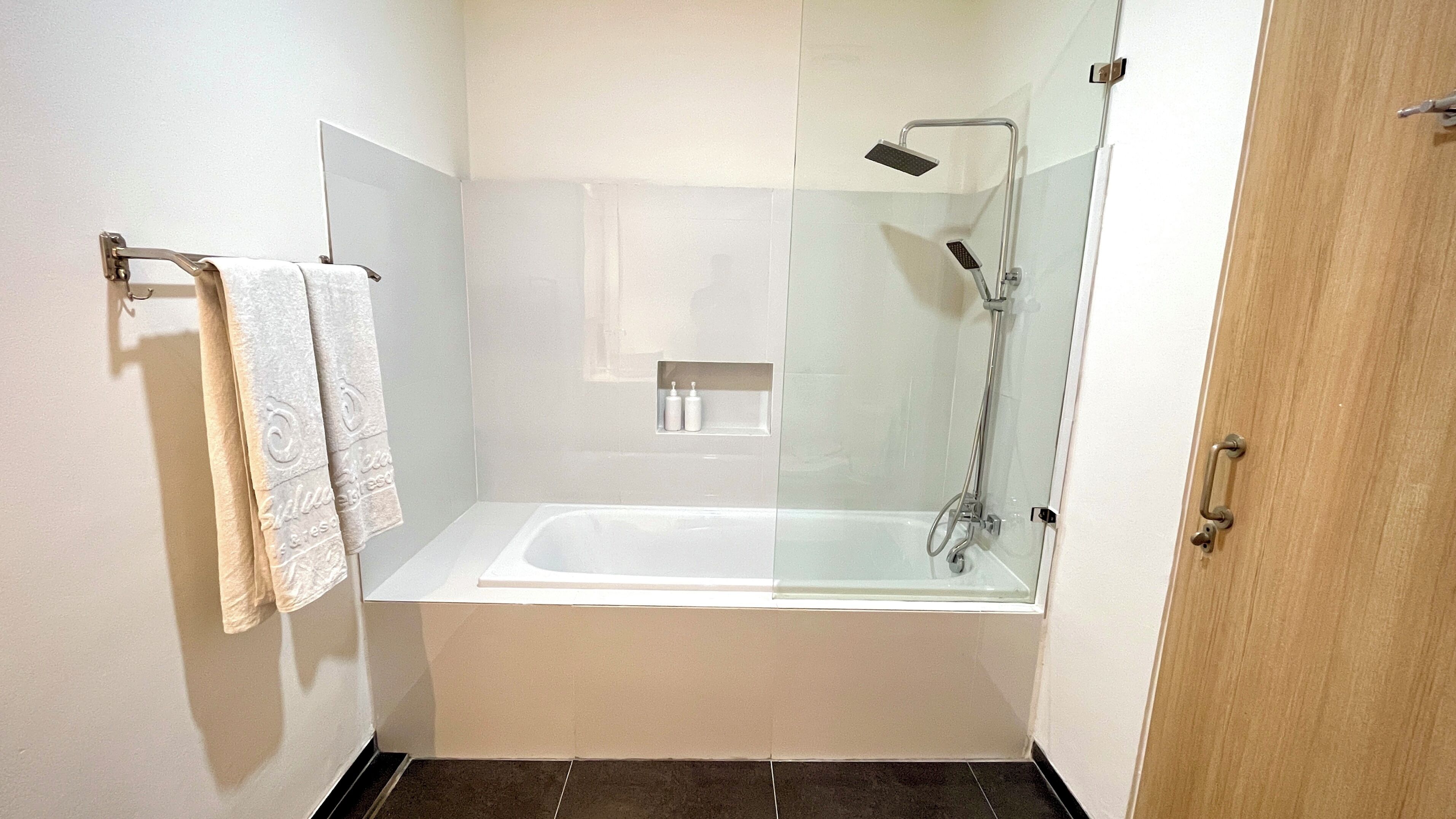 Un baño moderno con ducha envuelta en vidrio, una bañera blanca y un perchero con dos toallas.