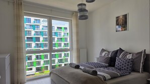 Une chambre avec une grande fenêtre, un lit recouvert d’une literie à motifs et un luminaire suspendu moderne.