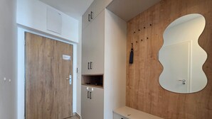 Un intérieur moderne avec une porte en bois, des armoires blanches, un banc et un miroir fixé au mur.