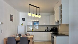 Une cuisine moderne avec des meubles blancs, une table à manger en bois et un plan de travail noir.