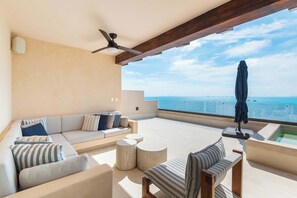 Une terrasse sur le toit, aménagée avec un canapé, des chaises, une table ronde, un ventilateur de plafond et offrant une vue sur la mer.
